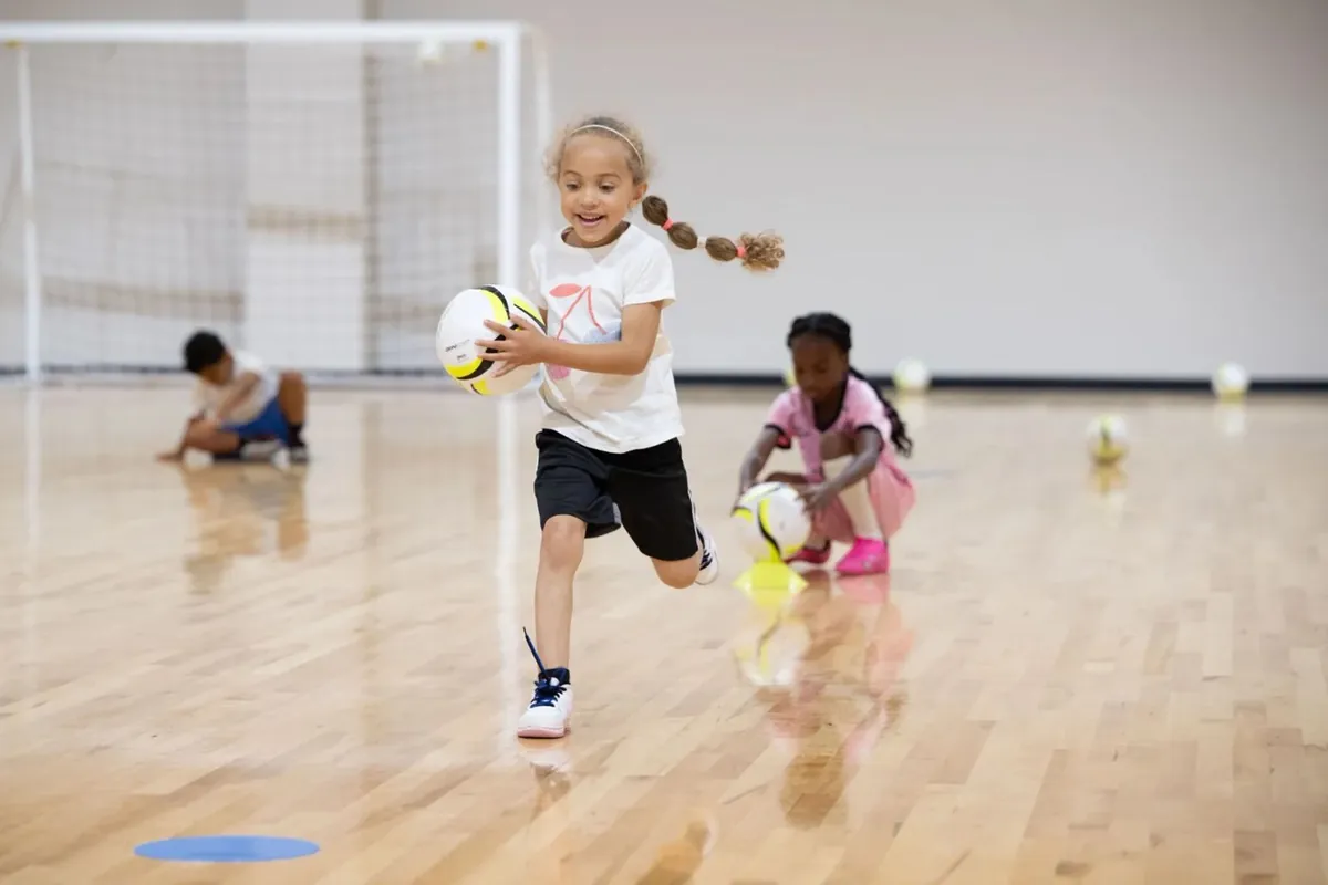 A girl dribbling a soccer ball in a school gym
